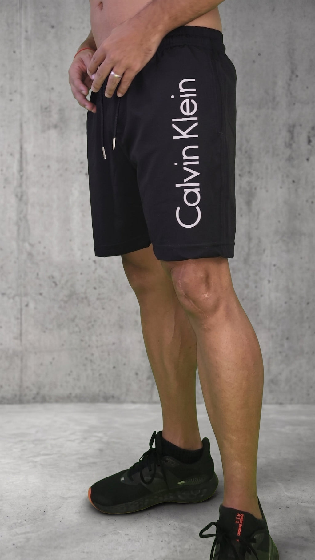 Pantaloneta negra para hombre con detalle tipográfico blanco vertical que dice Calvin Klein, vista lateral

