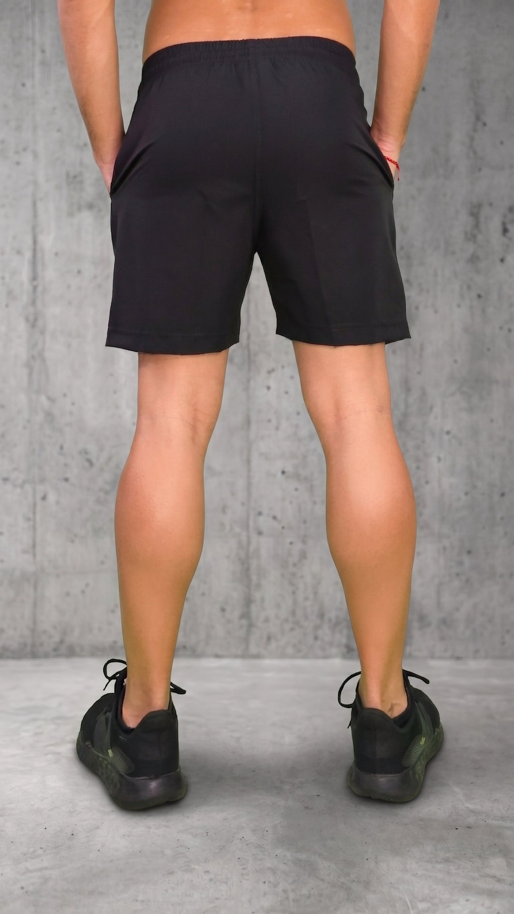 Pantaloneta negra para hombre vista desde atrás, con bloques laterales blanco y rojo, modelo con manos en los bolsillos