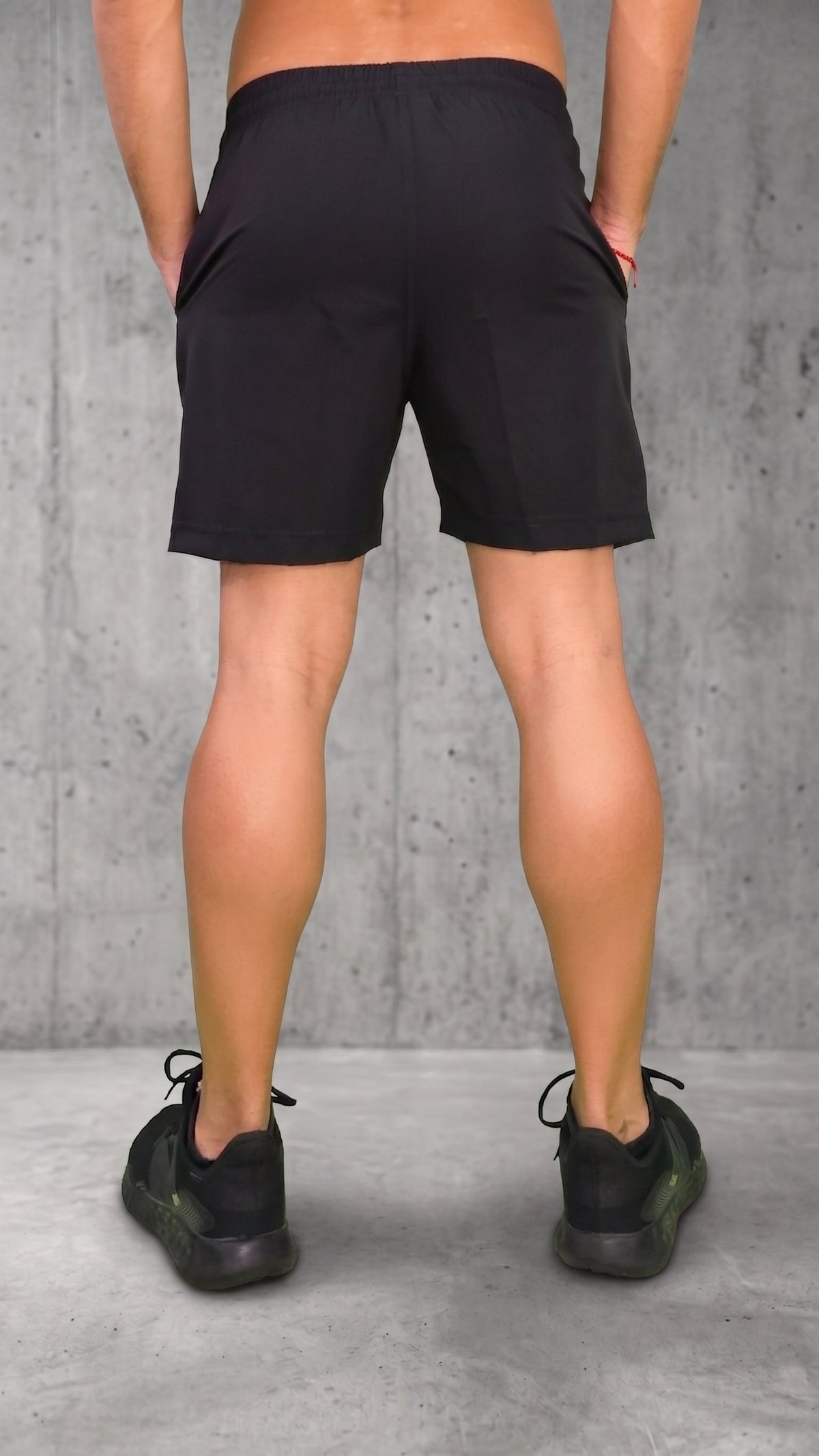 Pantaloneta negra para hombre vista desde atrás, con bloques laterales blanco y rojo, modelo con manos en los bolsillos